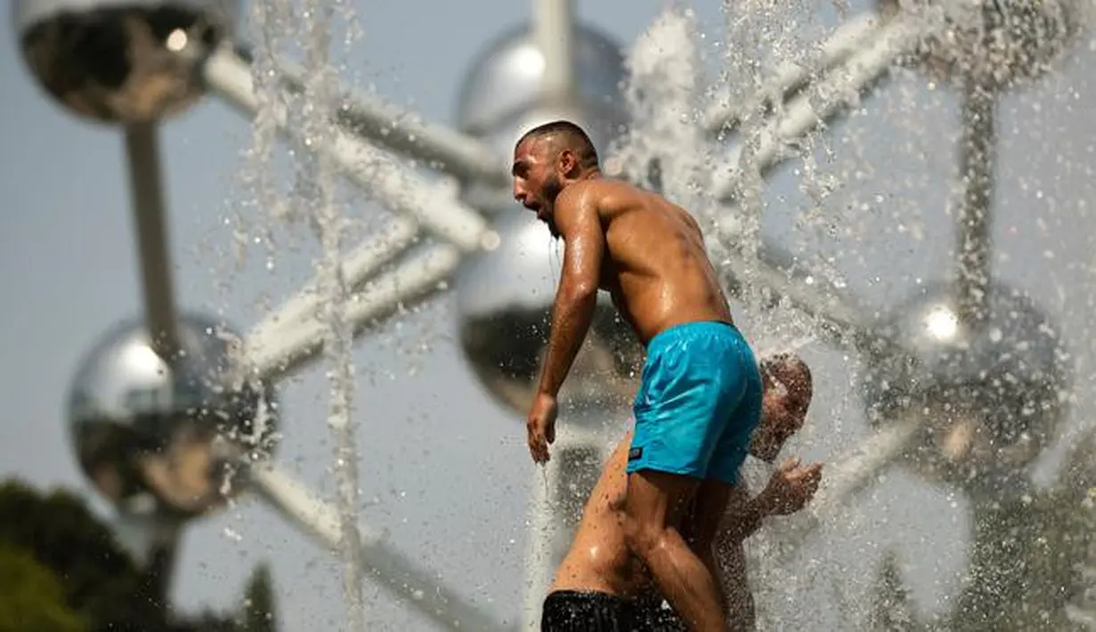 Dua pria mendinginkan diri dengan bermain di air mancur umum dekat Atomium saat gelombang panas melanda Eropa di Brussels, Belgia, Rabu (24/7/2019). Warga turun ke air mancur saat gelombang panas yang memecahkan rekor melanda Eropa. (AP Photo/Francisco Seco)