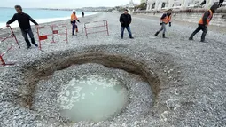 Petugas memasang paga besi mengelilingi kawah misterius berisi air payau yang muncul di Pantai Lido, Nice, Prancis, Kamis (1/2). Lubang selebar 5 meter dan sedalam 2 meter itu membuat banyak warga sekitar kebingungan. (VALERY HACHE/AFP)