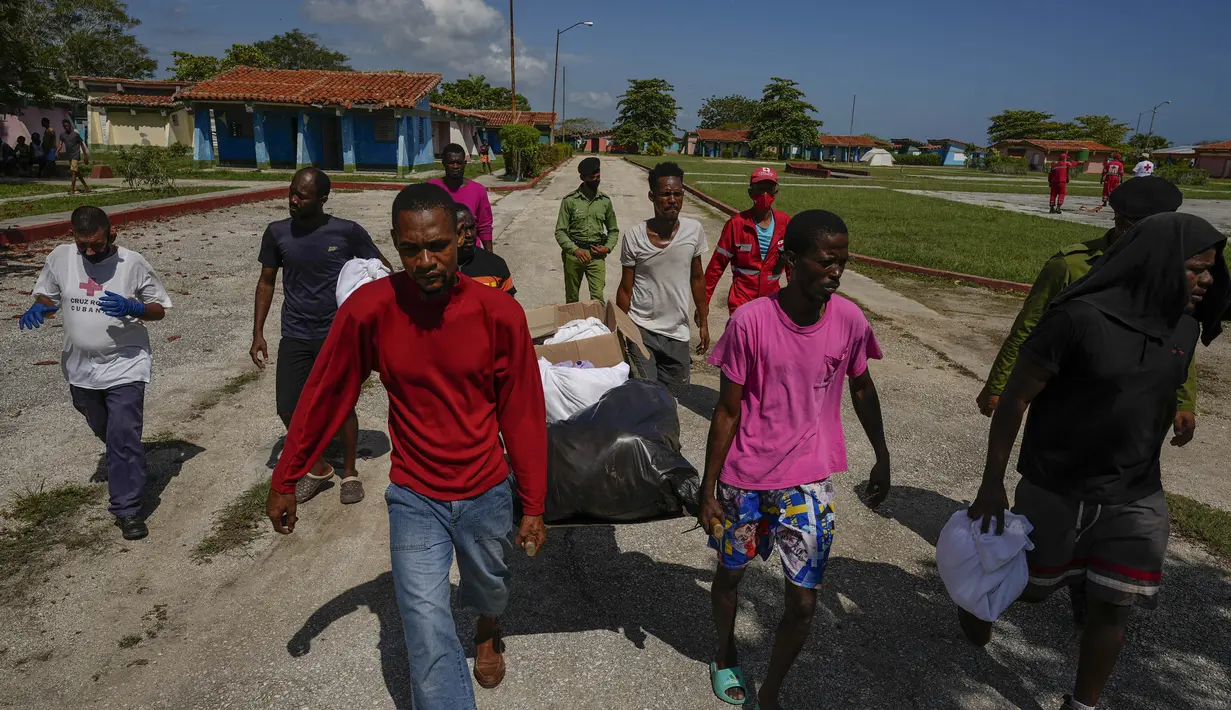Imigran Haiti membantu anggota Palang Merah mendistribusikan handuk dan perlengkapan mandi ke seluruh kelompok mereka di sebuah perkemahan yang digunakan untuk menampung sekelompok besar migran Haiti di Sierra Morena di provinsi Villa Clara Kuba, Kamis (26/5/2022). (AP Photo/Ramon Espinosa)