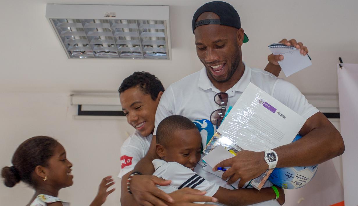 Mantan pemain sepak bola Didier Drogba memeluk anak-anak saat acara amal organisasi internasional Peace and Sport, di Cartagena, Kolombia (19/3). Didier Drogba merupakan pesebak bola dunia dari Pantai Gading. (Cesar Carrion/Colombian Presidency/AFP)