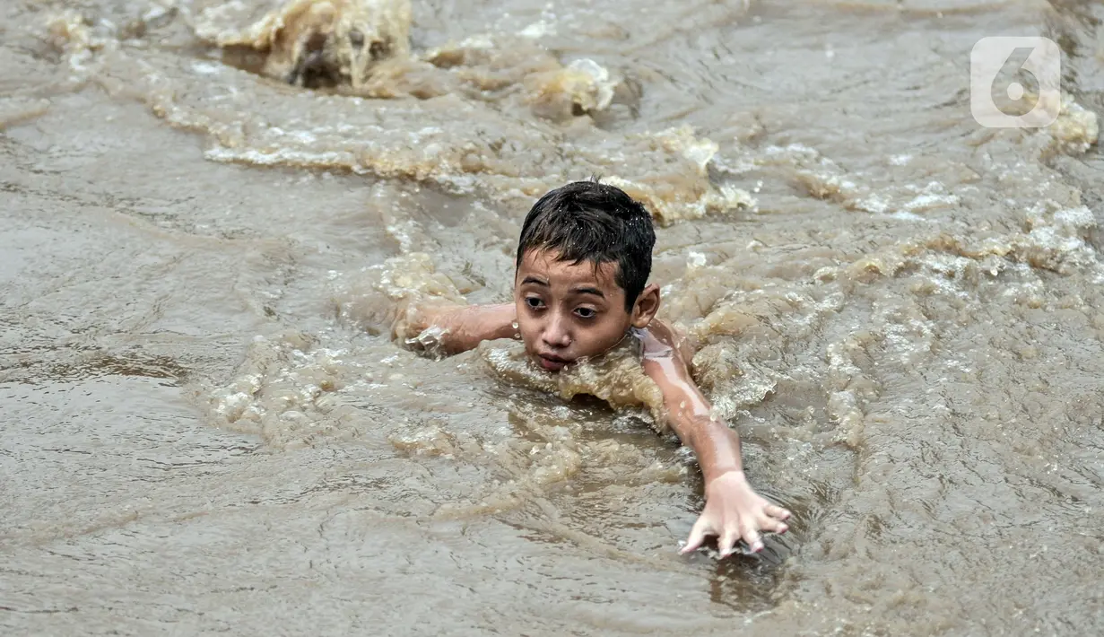 Seorang anak berenang di Kali Ciliwung yang meluap, Kebon Pala, Jatinegara, Jakarta Timur, Minggu (31/10/2021). Aliran Kali Ciliwung yang meluap akibat hujan di kawasan hulu dimanfaatkan anak-anak untuk berenang meski membahayakan keselamatan. (merdeka.com/Iqbal S. Nugroho)