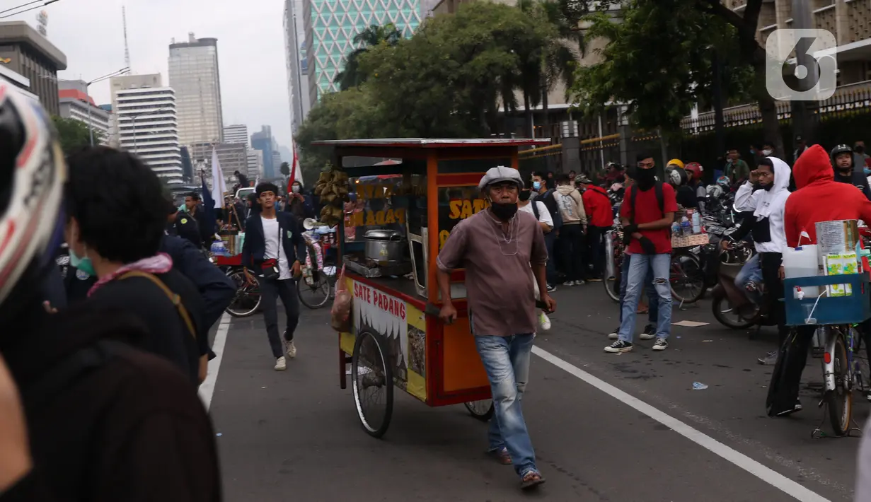 Pedangang menawarkan dagangannya kepada massa aksi saat demo penolakan omnibus law di kawasan patung kuda, Jakarta, Selasa (20/10/2020). Para pedagang kaki lima memanfaatkan moment aksi massa untuk mencari ke untungan meskupun sangat membahayakan bagi keselamatan mereka. (Liputan6.com/Angga Yuniar)