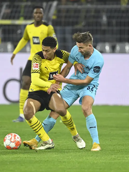 Gelandang Borussia Dortmund Jude Bellingham berebut bola dengan gelandang Greuther Fuerth Paul Seguin pada laga pekan ke-16 Bundesliga di Signal Iduna Park, Kamis (16/12/2021) dini hari WIB. Borussia Dortmund mampu meraih kemenangan 3-0 atas Greuther Fuerth. (Ina Fassbender/AFP)