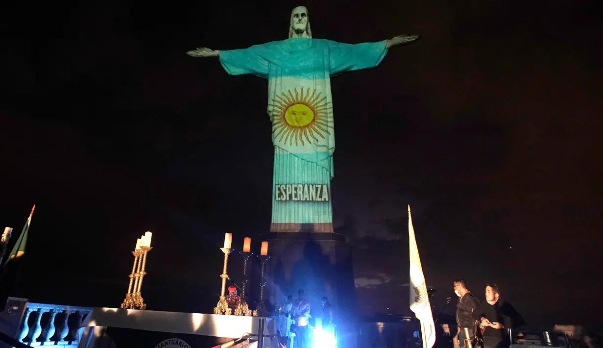Patung Christ the Redeemer atau Yesus sang Penebus yang populer di dunia menyala dengan gambar bendera Argentina selama pandemi Covid-19 di Rio de Janeiro, Brasil, Minggu (12/4/2020). Tubuh patung itu dipenuhi gambar negara-negara dengan wabah corona, sekaligus pesan dan harapan. (CARL DE SOUZA/AFP)