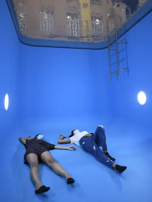 Pengunjung berfoto dengan instalasi "Kolam Renang" karya seniman Argentina Leandro Erlich di Belo Horizonte, Brasil, Senin (20/9/2021). Tampak ada orang tenggelam di bawah kolam renang ini, namun sebenarnya hanya ada lapisan air tipis di permukaan sehingga tak ada yang tenggelam. (DOUGLAS MAGNO/AFP)