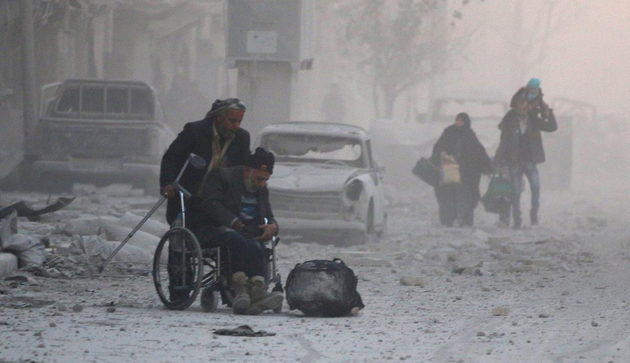 Seorang pria di kursi roda melarikan diri dengan sejumlah warga yang lain dari wilayah yang dikuasai pemberontak, Aleppo, Suriah (9/12). (REUTERS / Abdalrhman Ismail)