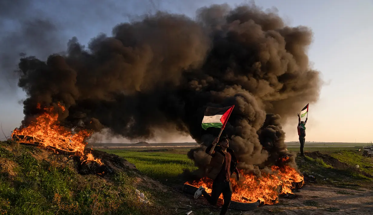 Warga Palestina membakar ban dan mengibarkan bendera nasional saat protes terhadap serangan militer Israel terhadap kamp pengungsi Jenin di perbatasan Israel-Palestina, sebelah timur Kota Gaza, 26 Januari 2023. Militer Israel mengatakan sedang melakukan operasi untuk menangkap militan ketika baku tembak meletus di kamp pengungsi Jenin. (AP Photo/Fatima Shbair)