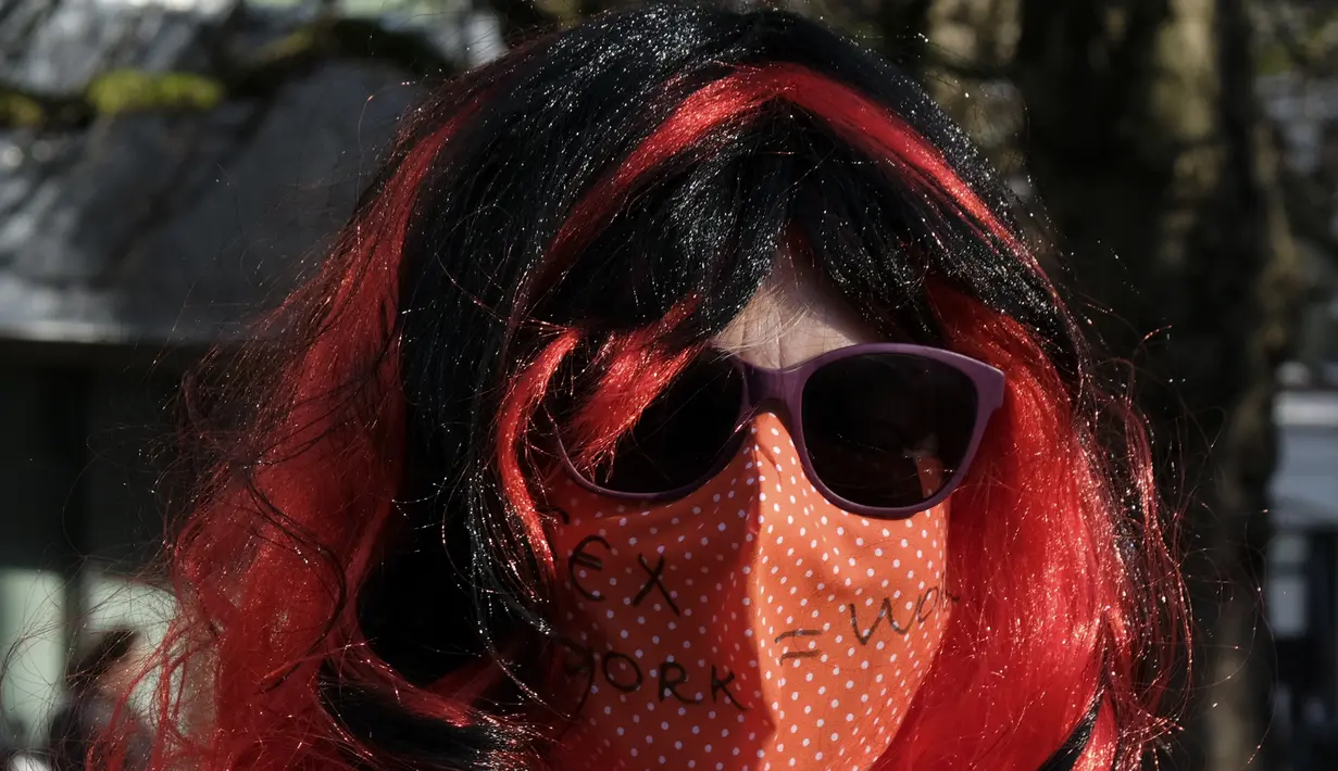 Seorang demonstran memakai masker bertuliskan "sex work = work" saat memprotes perlakuan dan stigma yang tidak setara di Den Haag, Belanda, Selasa (2/3/2021). Mereka berdemonstrasi di luar parlemen dalam protes terhadap penguncian keras virus corona oleh pemerintah. (AP Photo/Patrick Post)