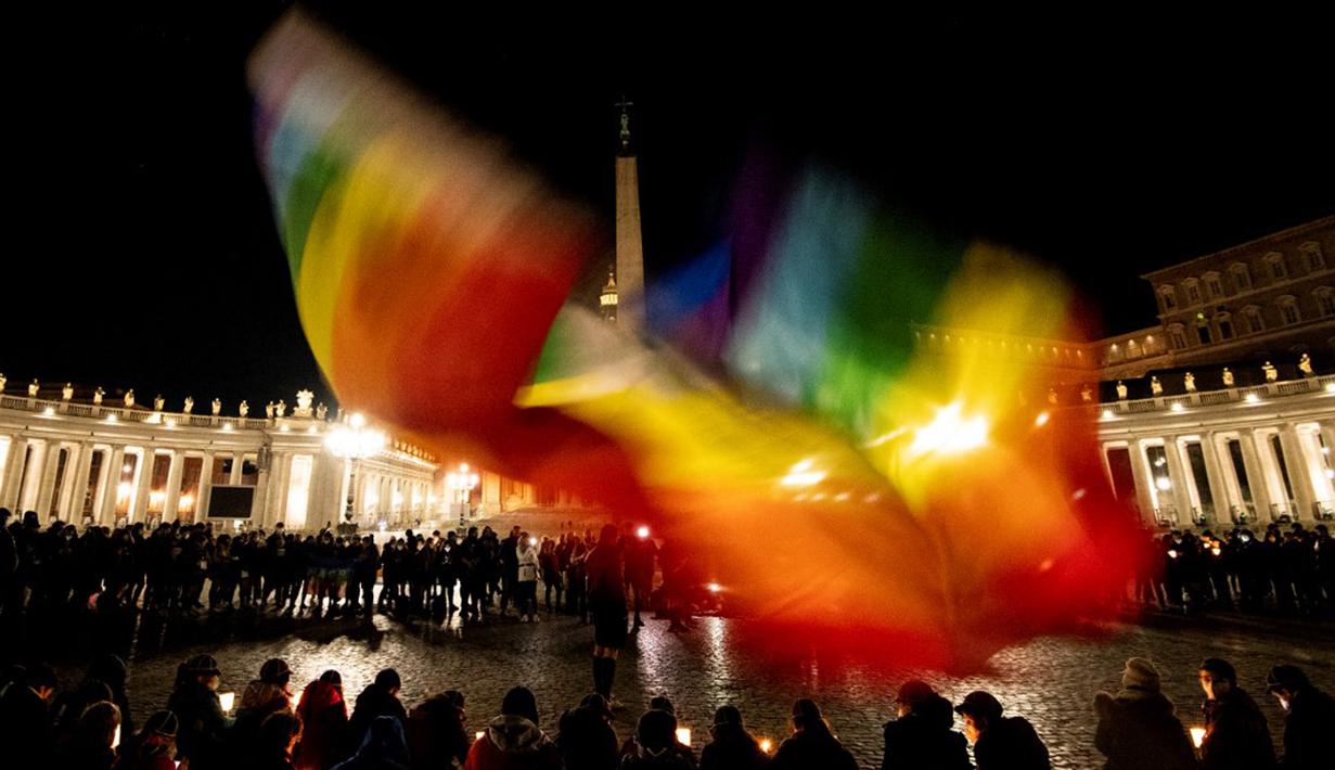 Seseorang mengibarkan bendera pelangi saat orang-orang yang percaya berdoa untuk perdamaian Ukraina di Lapangan Santo Petrus, Vatikan, 2 Maret 2022. (Tiziana FABI/AFP)