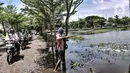 Rombongan pengantar jenazah melintas di dekat Amir yang tengah memancing di TPU Semper, Jakarta, Selasa (2/2/2021). Banjir tersebut dimanfaatkan warga setempat untuk mencari ikan dengan menggunakan alat pancing serta jala. (merdeka.com/Iqbal S. Nugroho)