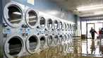 Pamela Cerruti berjalan melewati Pajaro Coin Laundry saat banjir mengelilingi mesin-mesin di komunitas Pajaro di Monterey County, California, Selasa, 14 Maret 2023.  (AP Photo/Noah Berger)
