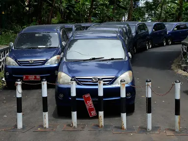 Pengendara motor melintasi deretan mobil dinas yang terparkir di area belakang Gedung DPR/MPR, Jakarta, Selasa (5/12).  Mobil-mobil berplat merah tersebut dibiarkan mangkrak hingga berkarat lantaran menunggu proses lelang. (Liputan6.com/Johan Tallo)
