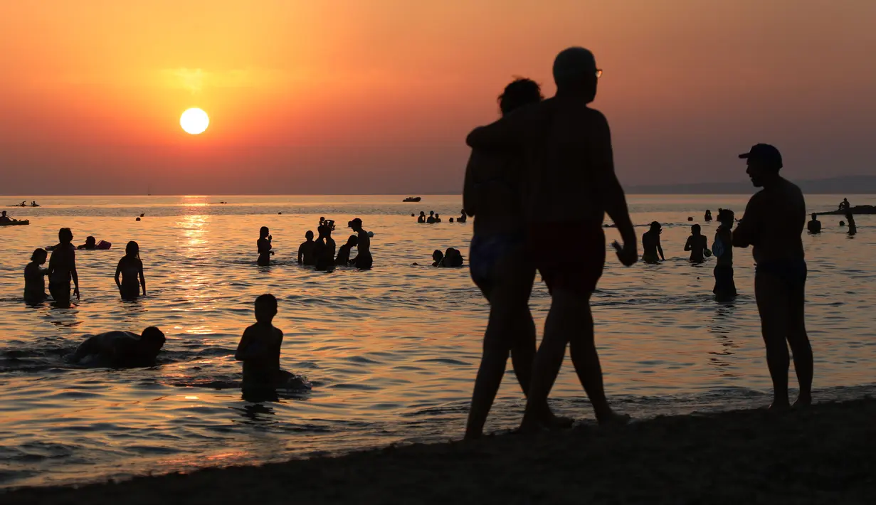 Pengunjung berenang sambil menikmati pemandangan matahari terbenam di Pantai Santa Maria Del Focalo, Pulau Sisilia, Italia, 7 Agustus 2017. Pantai Santa Maria Del Focalo menjadi salah satu tujuan objek wisata favorit di Italia. (ludovic MARIN/AFP)