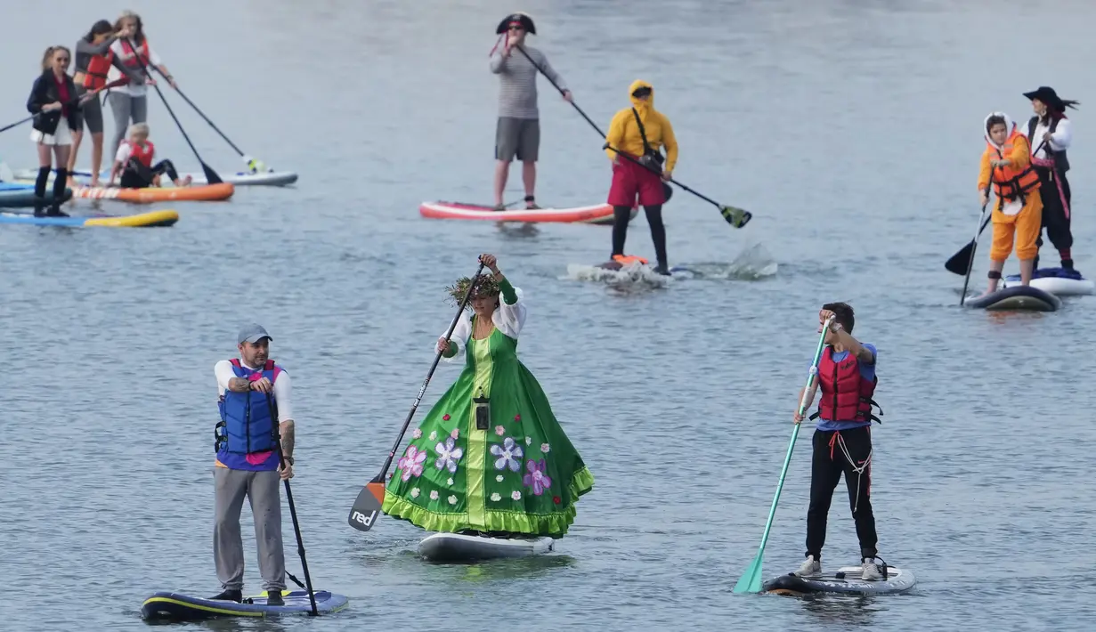 Orang-orang mengarahkan papan SUP mereka selama festival dayung berdiri (stand up paddle) di kanal dayung Olimpiade Krylatskoye, Moskow, Rusia, Minggu (12/9/2021). Festival dihadiri para peserta dalam balutan kostum warna-warni yang menggambarkan aneka karakter dalam tokoh film. (AP/Pavel Golovkin)