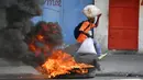 Seorang pria berlari melewati ban yang dibakar oleh pengunjuk rasa yang kesal dengan meningkatnya kekerasan di lingkungan Lalue, Port-au-Prince, Haiti, Rabu (14/7/2021). Presiden Haiti Jovenel Moise dibunuh pada 7 Juli. ( AP Photo/Fernando Llano)