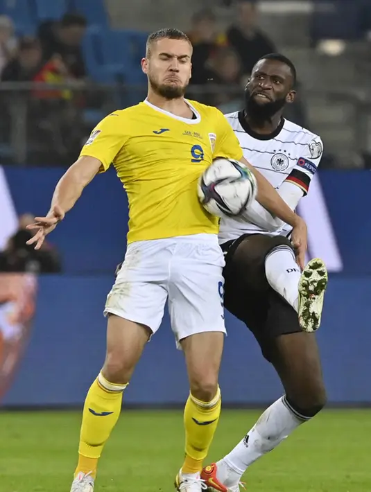 Pemain Rumania George Puscas (kiri) berebut bola dengan pemain Jerman Antonio Ruediger pada pertandingan Grup J kualifikasi Piala Dunia Qatar 2022 di Hamburg, Jerman, 8 Oktober 2021. Jerman menang 2-1. (John MACDOUGALL/AFP)