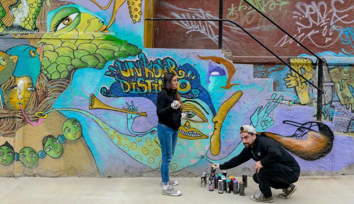 Seniman Sammy Espinosa (kanan) dan istrinya Cynthia Aguilera menyelesaikan pembuatan mural jalanan di Valparaiso, Chile, 9 April 2019. Mereka menamai kelompoknya Un Kolor Distinto (warna yang berbeda). (Martin BERNETTI/AFP)