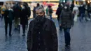 Seorang pejalan kaki, mengenakan masker, berdiri di depan pohon natal di jalan Roma, Italia pada Kamis (23/12/2021). Pemerintah Italia telah mewajibkan kembali penggunaan masker di luar ruangan untuk menahan peningkatan kasus Covid-19 yang didorong oleh varian Omicron. (Filippo MONTEFORTE/AFP)