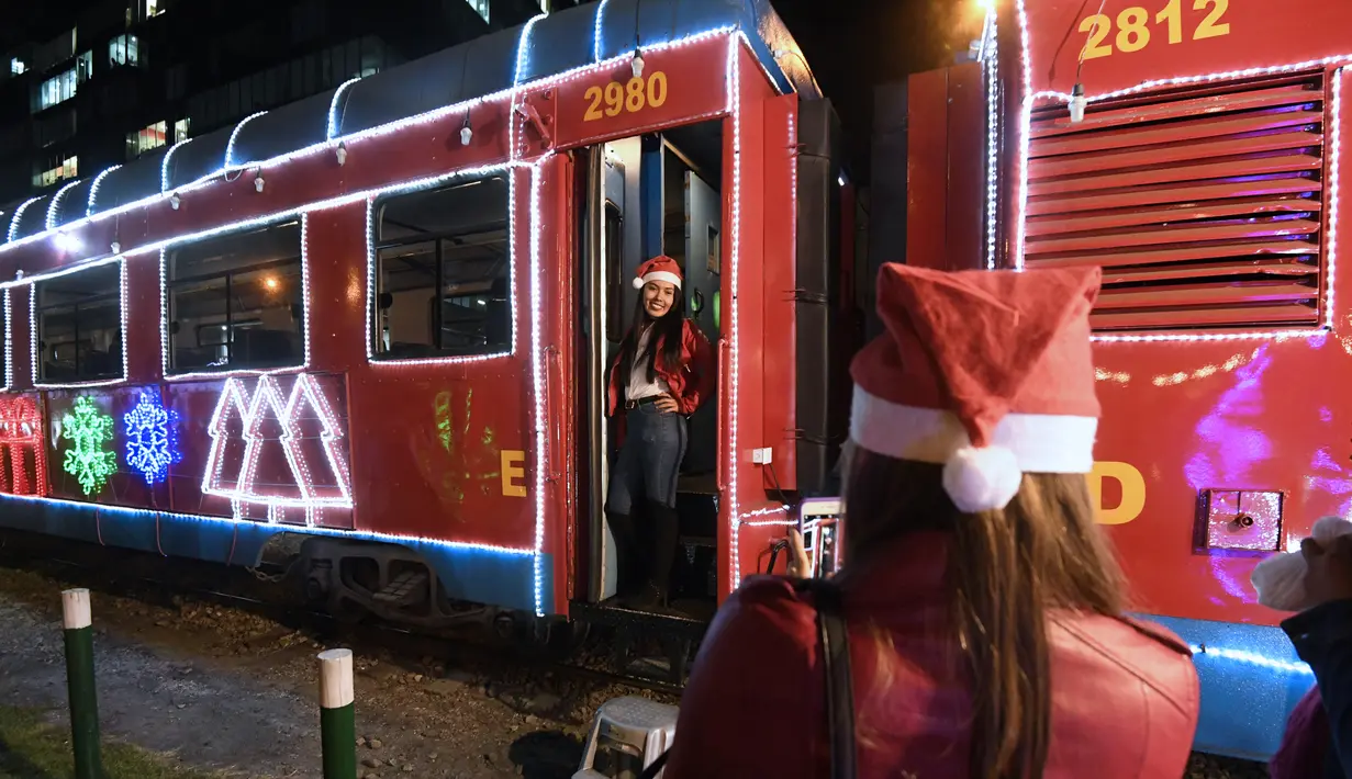Seorang wanita berpose di kereta wisata yang dihiasi lampu Natal di Bogota (20/12/2019). Meyambut Hari Natal, kereta wisata di Kolombia membuat cara unik dengan memasangkan lampu warna-warni agar menjadi daya tarik penumpang. (AFP Photo/Juan Barreto)