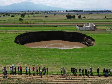 Pemandangan udara dari sinkhole yang ditemukan oleh petani di lahan pertanian di Santa Maria Zacatepec, negara bagian Puebla, Meksiko pada 30 Mei 2021. Lubang yang penuh dengan air itu pada hari Minggu lebarnya hanya sekitar 30 meter. (JOSE CASTAÑARES/AFP)