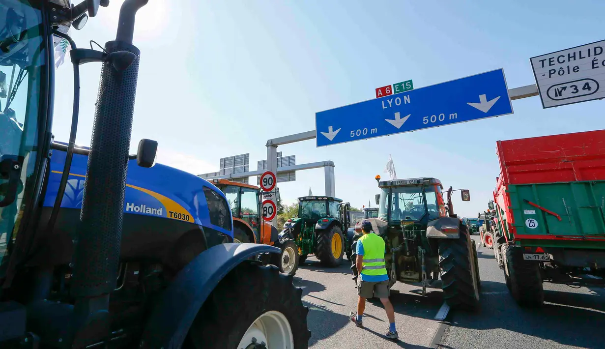 Seorang warga berjalan di tengah traktor  di jalan raya A6 di Limonest, dekat Lyon, Prancis (23/7/2015). Petani Perancis memprotes kembali ketidak seimbangan keuntungan yang diperoleh antara petani dan pengecer. (REUTERS/Robert Pratta)