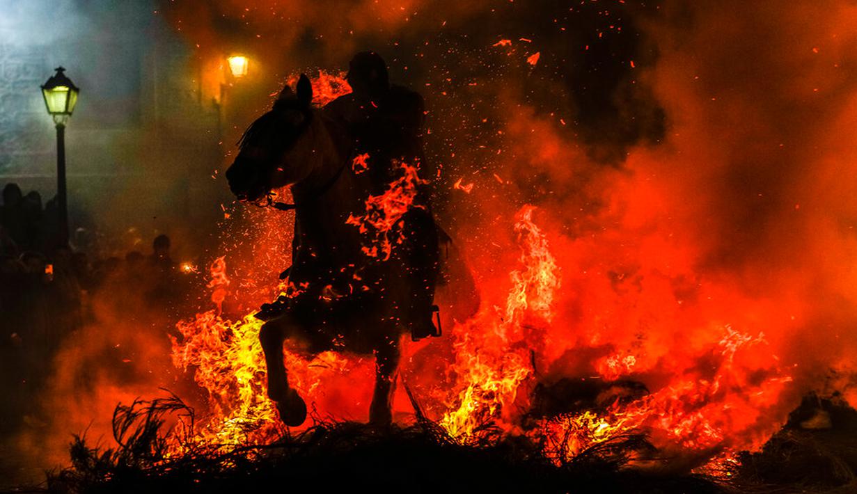<p>Seorang pria menunggang kuda melintasi kobaran api dalam tradisi tahunan Luminarias memperingati Hari Santo Anthony (santo pelindung hewan) di San Bartolome de Pinares, Spanyol, 16 Januari 2023. Tradisi yang sudah berlangsung selama 500 tahun ini dilakukan sebagai upaya 'pemurnian' hewan dengan cara melintasi kobaran api. (AP Photo/Manu Fernandez)</p>