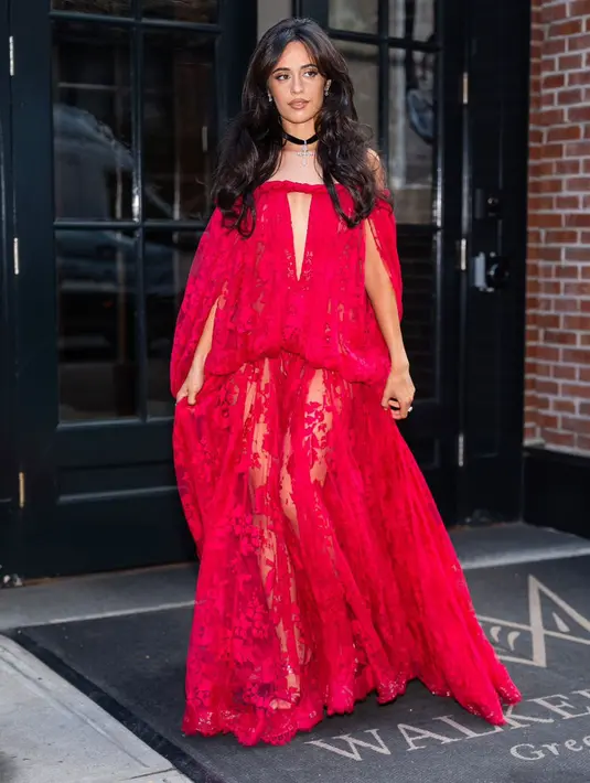 Camila Cabello tampil paling berani lewat gaun merah fuchsia menyala berbahan lace transparan dengan siluet cape yang menjuntai hingga lantai. Detail cut-out di bagian dada dan permainan tekstur membuat penampilannya terlihat teatrikal sekaligus sensual. Rambut bergelombang dan choker berliontin melengkapi gaya gothic romantic yang mencuri perhatian.