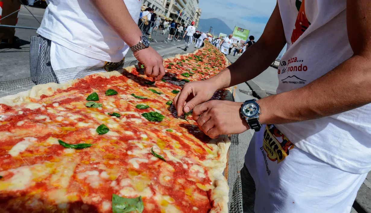 Koki ahli saat menyelesaikan pembuatan pizza terpanjang untuk mencetak rekor dunia, di sepanjang pinggir Laut Naples, Italia, 18 Mei 2016. Pizza itu memiliki ukuran sekitar 1 mil dan terbentang di sepanjang pinggir Laut Naples. (Mario LAPORTA/AFP)