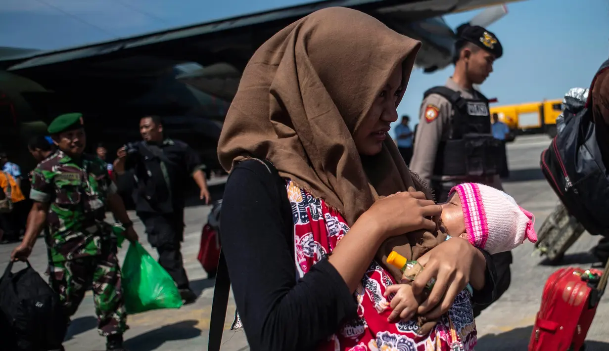 Seorang wanita membawa anaknya ketika mereka tiba di Surabaya, Kamis (4/10). Banyak anak-anak yang terpisah dari keluarganya setelah bencana gempa-tsunami melanda Palu dan Donggala pada 28 September. (AFP Photo/Juni Kriswanto)