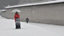 Seorang wanita mengendarai kursi dorong di sepanjang jalan yang tertutup salju di pusat kota Seoul (19/1/2022). Peringatan salju tebal telah dikeluarkan di seluruh kota pada pukul 9 pagi. (AFP/Jung Yeon-je)