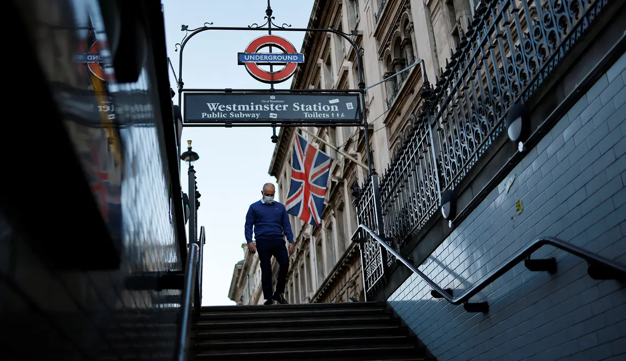 Seorang anggota masyarakat yang mengenakan masker untuk mengurangi penyebaran Covid-19, berjalan di bawah bendera Union saat memasuki Stasiun Westminster di London pusat (5/1/2022). Kasus Covid-19 harian negara itu menembus 200.000 untuk pertama kalinya. (AFP/Tolga Akmen)