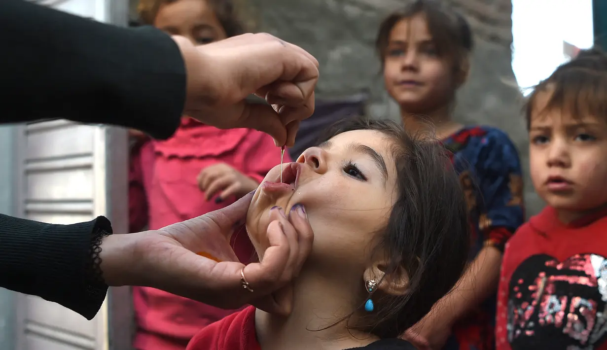 Tenaga kesehatan (kiri) memberikan vaksin polio kepada seorang anak selama kampanye vaksinasi di kawasan tua Kabul, Afghanistan pada 8 November 2021. Vaksinasi tersebut merupakan yang pertama sejak Taliban berkuasa di Afghanistan. (WAKIL KOHSAR / AFP)