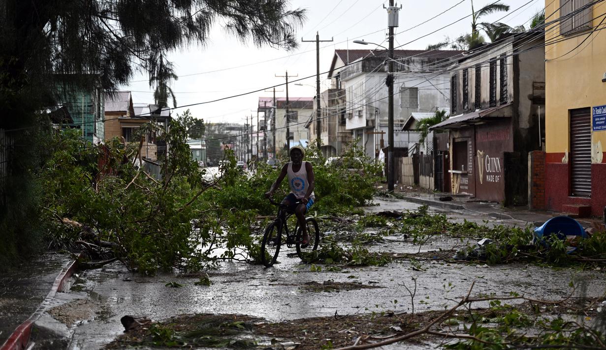 Seorang pria bersepeda melewati jalan yang terhalang oleh cabang-cabang pohon tumbang setelah Badai Lisa di Ladyville, dekat Belize City, Belize, 3 November 2022. Badai Tropis Lisa menyebabkan banjir dan membuat sebagian negara itu menjadi gelap gulita. (Johan ORDONEZ/AFP)