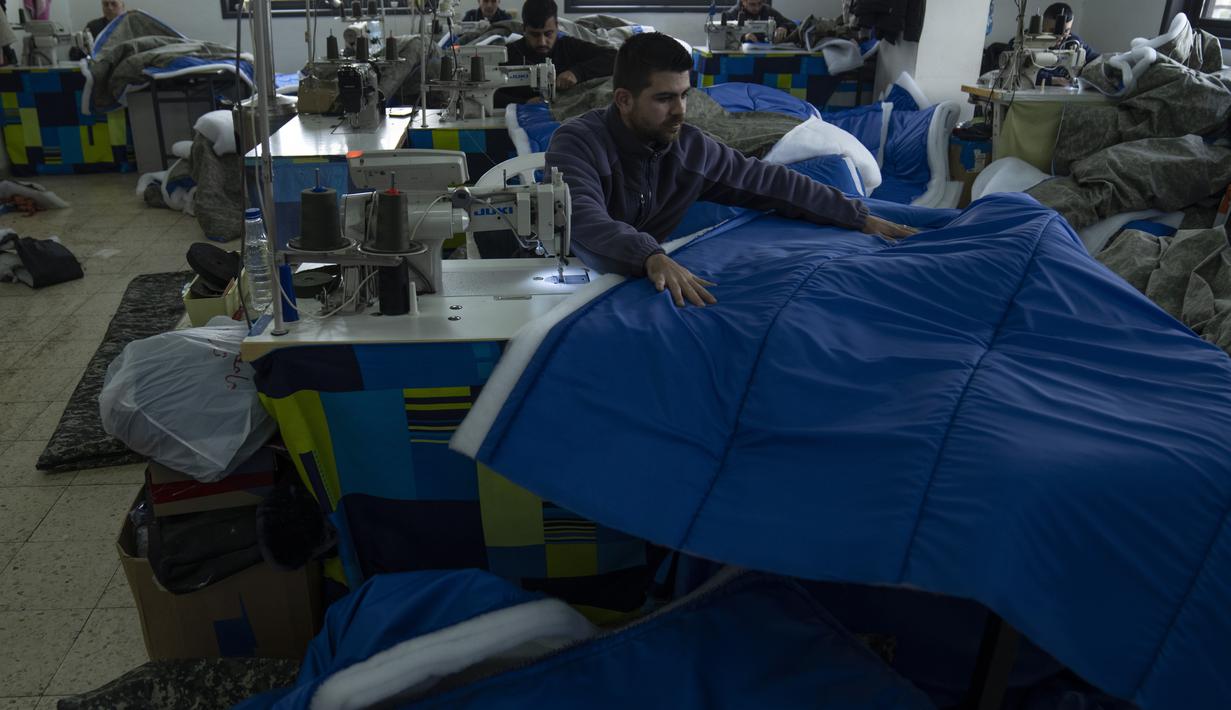 Penjahit memproduksi dan menyiapkan pengiriman massal perlengkapan tidur untuk korban gempa bumi di Turki dan Suriah yang sekarang terkena cuaca musim dingin yang membekukan, di sebuah pabrik Palestina di kota Hebron, Tepi Barat, Kamis (16/2/2023).  Diketahui, gempa bumi mengguncang Turki dan Suriah dengan magnitudo 7,8 pada Senin (6/2/2023). Guncangan gempa itu diikuti oleh ratusan gempa susulan. (AP Photo/Nasser Nasser)