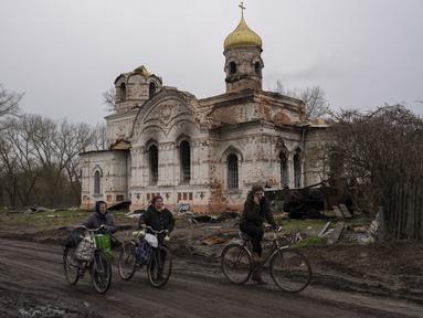 Warga berjalan dengan sepeda mereka di depan sebuah gereja yang rusak, di Lukashivka, di utara Ukraina, 22 April 2022. Penduduk mengatakan tentara Rusia menggunakan rumah ibadah untuk menyimpan amunisi, dan pasukan Ukraina menembaki gedung itu untuk membuat Rusia pergi. (AP Photo/Petros Giannakouris)