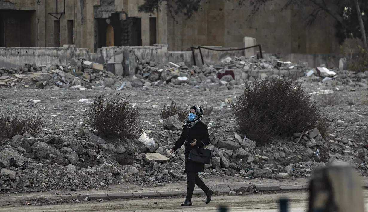 Seorang perempuan mengenakan masker berjalan melewati puing-puing di kota Raqa, bekas ibu kota ISIS, di Suriah utara pada 20 Desember 2020. Raqqa menjadi saksi terusirnya anggota kelompok ekstremis oleh Pasukan Demokratik Suriah pada Oktober 2017 lalu. (Photo by Delil SOULEIMAN / AFP)