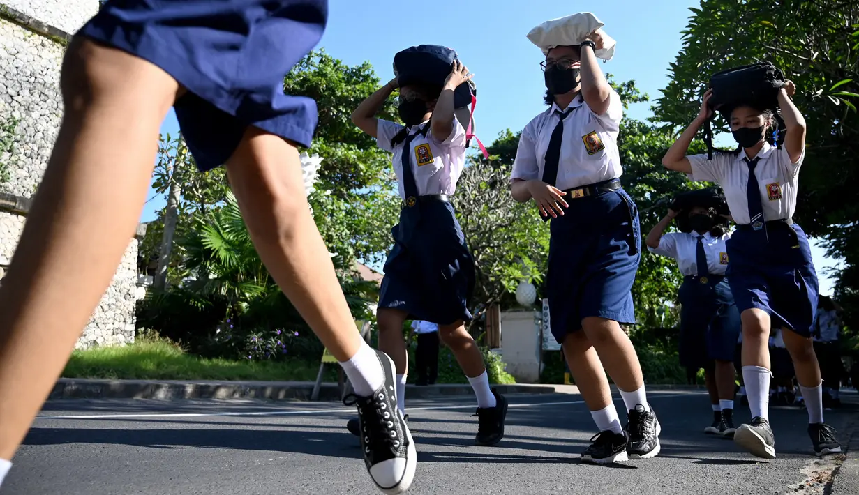Anak-anak sekolah menggunakan tas mereka untuk melindungi diri saat latihan gempa dan tsunami di Tanjung Benoa, Kabupaten Badung, Bali, 24 Mei 2022. (SONY TUMBELAKA/AFP)