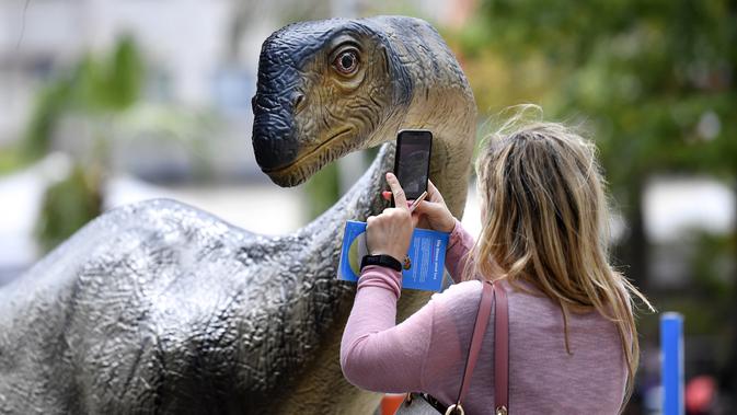 Seorang wanita mengambil foto replika dinosaurus Europasaurus seukuran aslinya di pusat kota Bochum, Jerman (12/8/2019). Jejak dinosaurus berumur 316 juta tahun ditemukan di lubang batu di kota itu enam tahun lalu di kota ini. (AP Photo/Martin Meissner)