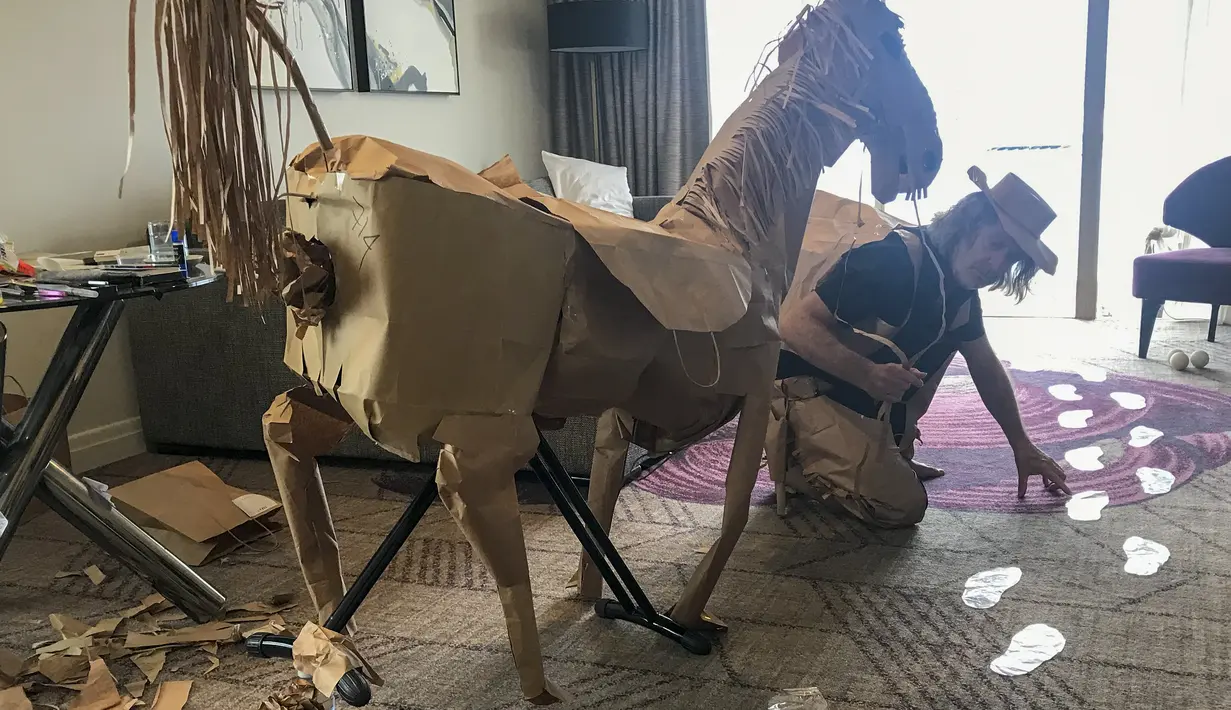 David Marriott berpose dengan kuda kertasnya Russell di kamar hotelnya di Brisbane, Australia, 3 April 2021. Saat berada dalam kamar hotel untuk karantina, direktur seni di iklan TV itu bosan dan mulai membuat pakaian koboi dari kantong kertas makanannya yang dikirimkan. (David Marriott via AP)