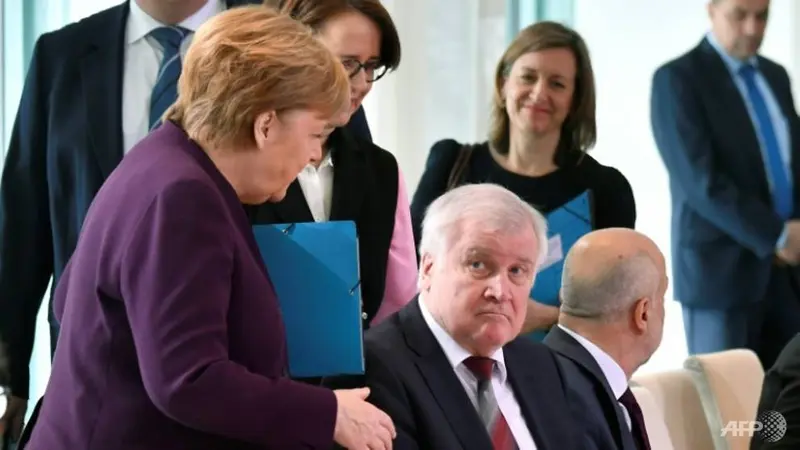 Angela Merkel mengulurkan tangan untuk menyambut Horst Seehofer pada sebuah pertemuan tentang migrasi di Berlin.