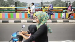 Pejalan kaki melintasi jembatan layang yang dicat dengan warna-warna ceria di Kampung Makasar, Jakarta, Kamis (26/7).  Pengecatan dilakukan guna mempercantik dan menyambut Asian Games 2018 pada Agustus mendatang.  (Liputan6.com/Faizal Fanani)