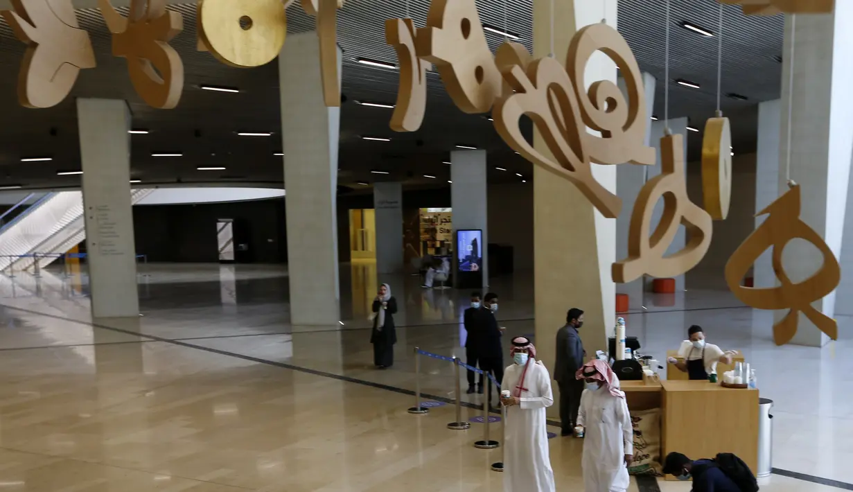 Warga Saudi berjalan di bawah guntingan huruf Arab yang menghiasi Pusat Kebudayaan Dunia Raja Abdulaziz, juga dikenal sebagai Ithra, di Dammam, Arab Saudi, Minggu (27/6/2021).  Pusat ini dibangun oleh Saudi Aramco dan diresmikan oleh Raja Salman pada 2016. (AP Photo/Amr Nabil)