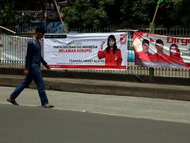 Pejalan kaki berjalan di depan spanduk partai politik yang terpampang di Jalan Sultan Agung, Manggarai, Jakarta, Selasa (16/1). Memasuki 2018, parpol berlomba mengambil hati rakyat dengan berbagai janji terpampang di spanduknya. (Liputan6.com/JohanTallo)