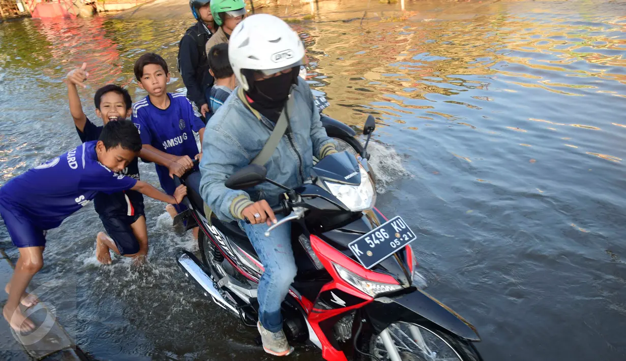 Anak-anak membantu pengendara motor untuk melintasi jalan yang tergenang banjir rob di ruas jalur pantura Semarang-Demak ,Jawa Tengah, Minggu (12 /06/2016). Meski banjir yang cukup tinggi hanya kendaraan besar truk atau bus yang bisa melintas. (Gholib)