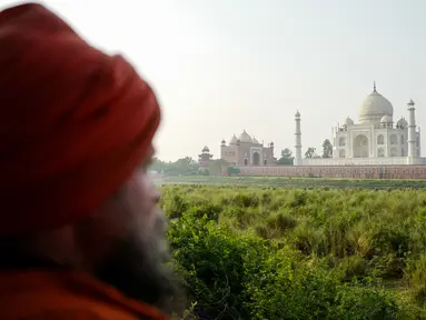Seorang pria berdiri di seberang Taj Mahal dari tepi sungai Yamuna di Agra, Jumat (4/5). India tengah dirundung kekhawatiran akan perubahan warna pada salah satu situs bersejarah dunia, Taj Mahal karena terpapar polusi. (AFP/CHANDAN KHANNA)