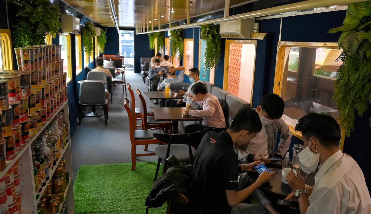 Foto yang diambil pada 31 Mei 2021 menunjukkan orang-orang duduk di dalam sebuah kafe, dari gerbong kereta, di stasiun kereta api di Phnom Penh. Gerbong kereta diubah menjadi kafe setelah selama pandemi corona sebagian besar perjalanan kereta api di Kamboja dihentikan. (TANG CHHIN Sothy/AFP)