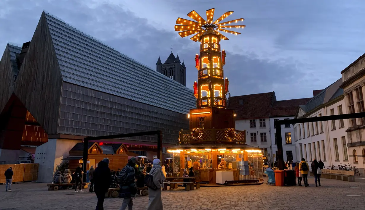 Orang-orang berjalan dekat pasar Natal kecil di shopping street di Ghent, Belgia, Rabu (22/12/2021). Mulai hari Minggu, pihak berwenang telah memutuskan menutup bioskop, teater dan ruang konser, sementara penggemar olahraga akan dilarang masuk stadion dan aula dalam ruangan. (AP Photo/Virginia Mayo)