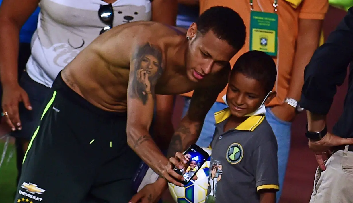 Pemain Brasil, Neymar Junior berfoto selfie bersama seorang anak kecil pada sesi latihan di Salvador, Brasil, Senin(16/11/2015). Brasil akan melawan Peru pada Qualifikasi Piala Dunia Rusia 2018. AFP Photo/Christophe Simon)