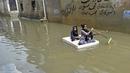 Gadis-gadis menggunakan rakit sementara melintasi jalan yang banjir di daerah perumahan setelah hujan muson lebat di Karachi (26/7/2022). Keadaan darurat cuaca diumumkan di Karachi karena hujan muson yang lebih deras dari biasanya terus melanda kota terbesar di Pakistan, membanjiri rumah-rumah dan membuat jalan-jalan tidak dapat dilalui. (AFP/Rizwan Tabassum)