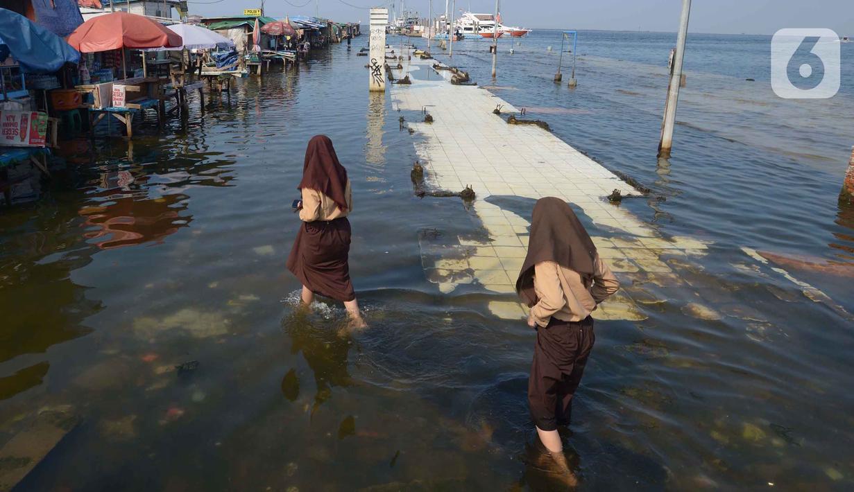 Siswi melintasi banjir rob di Pelabuhan Kali Adem, Muara Angke Jakarta, Rabu (5/1/2022). Menurut BMKG, adanya fase bulan baru yang bersamaan dengan masa Perigee (jarak terdekat bulan bumi) menyebabkan peningkatan signifikan ketinggian pasang air laut mencapai maksimum. (merdeka.com/Imam Buhori)